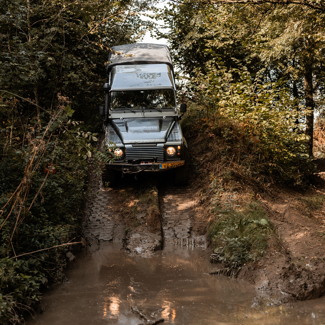 Landrover rijdt van heuvel af richting plas tijdens een teambuildingsdag
