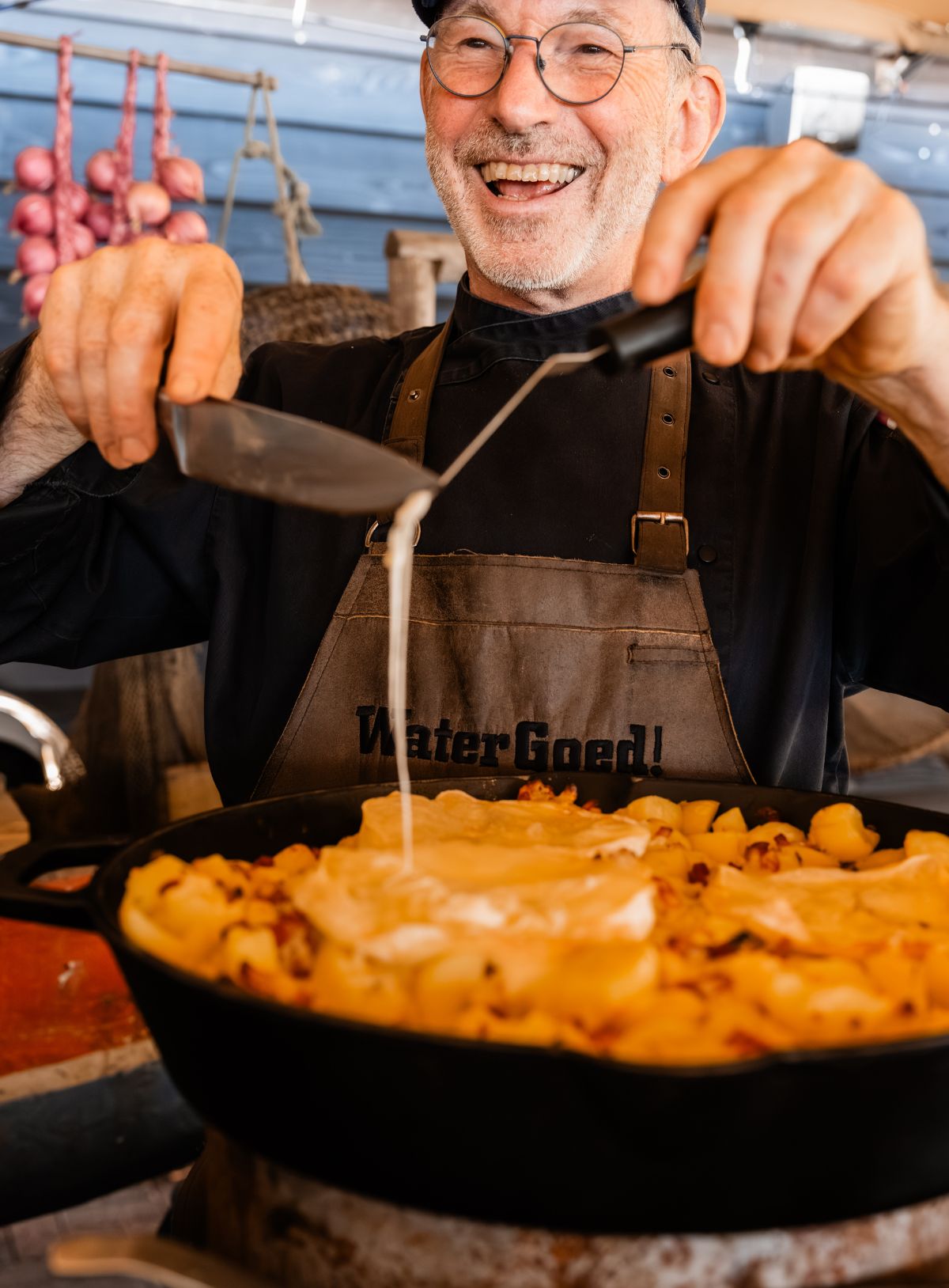 Lachende chef die laat zien hoe de kaas gesmolten is op Tartiflette recept